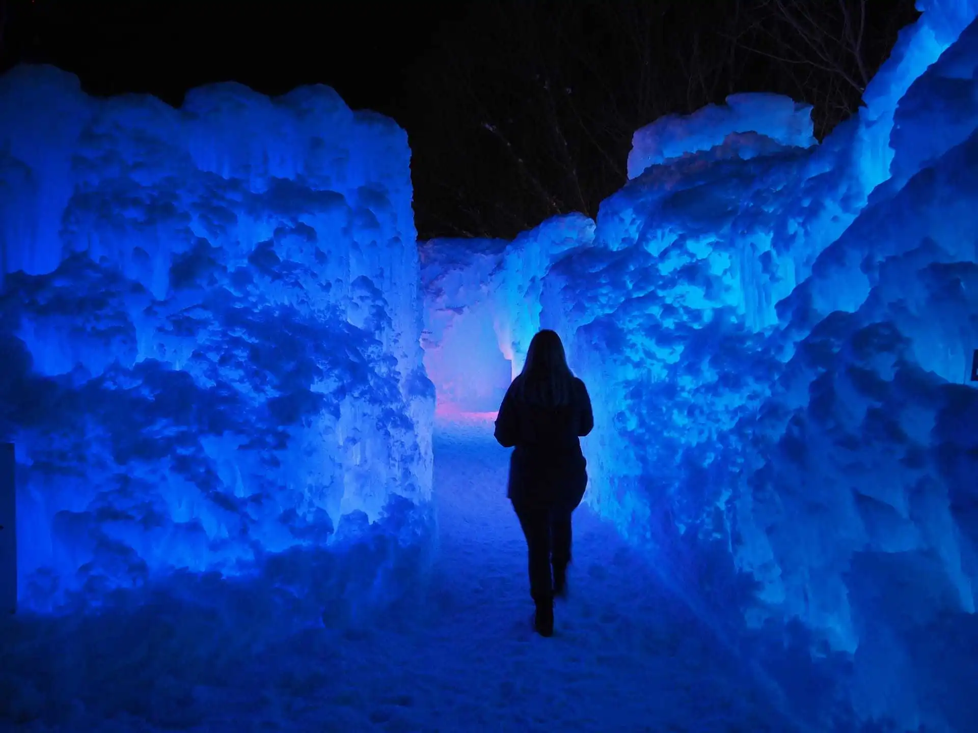 Lindsey walks through an ice castle that is backlit with beautiful blue and purple lighting