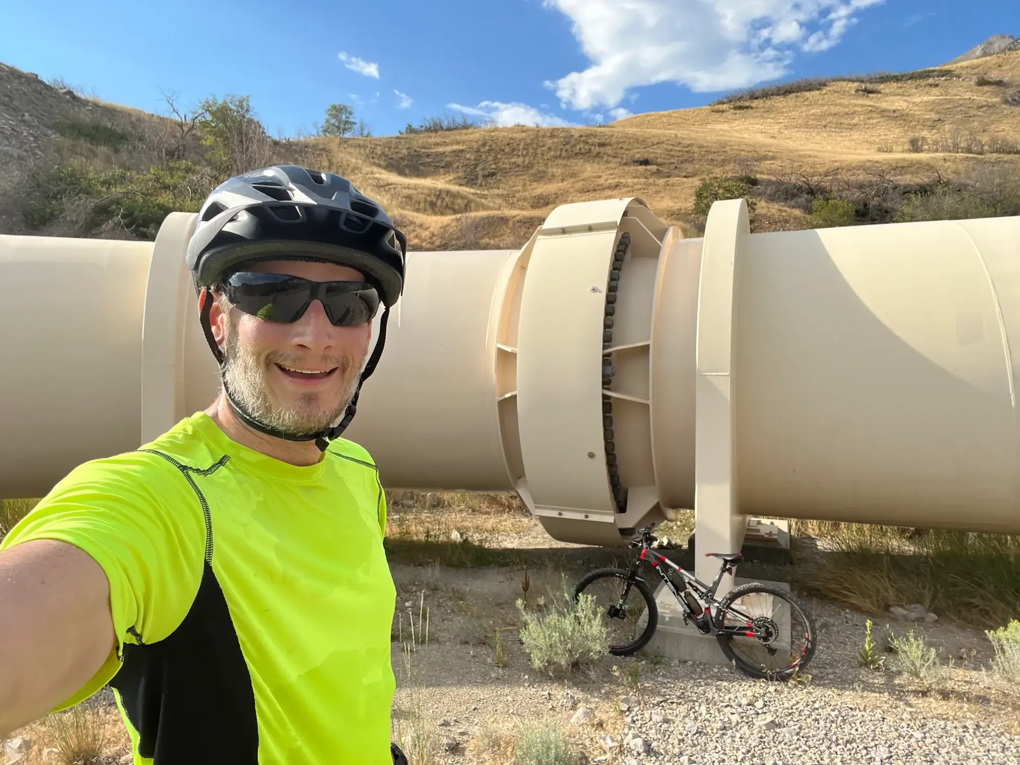 Keith is taking a selfie with his bike in front of a huge water pipe in Provo Canyon.