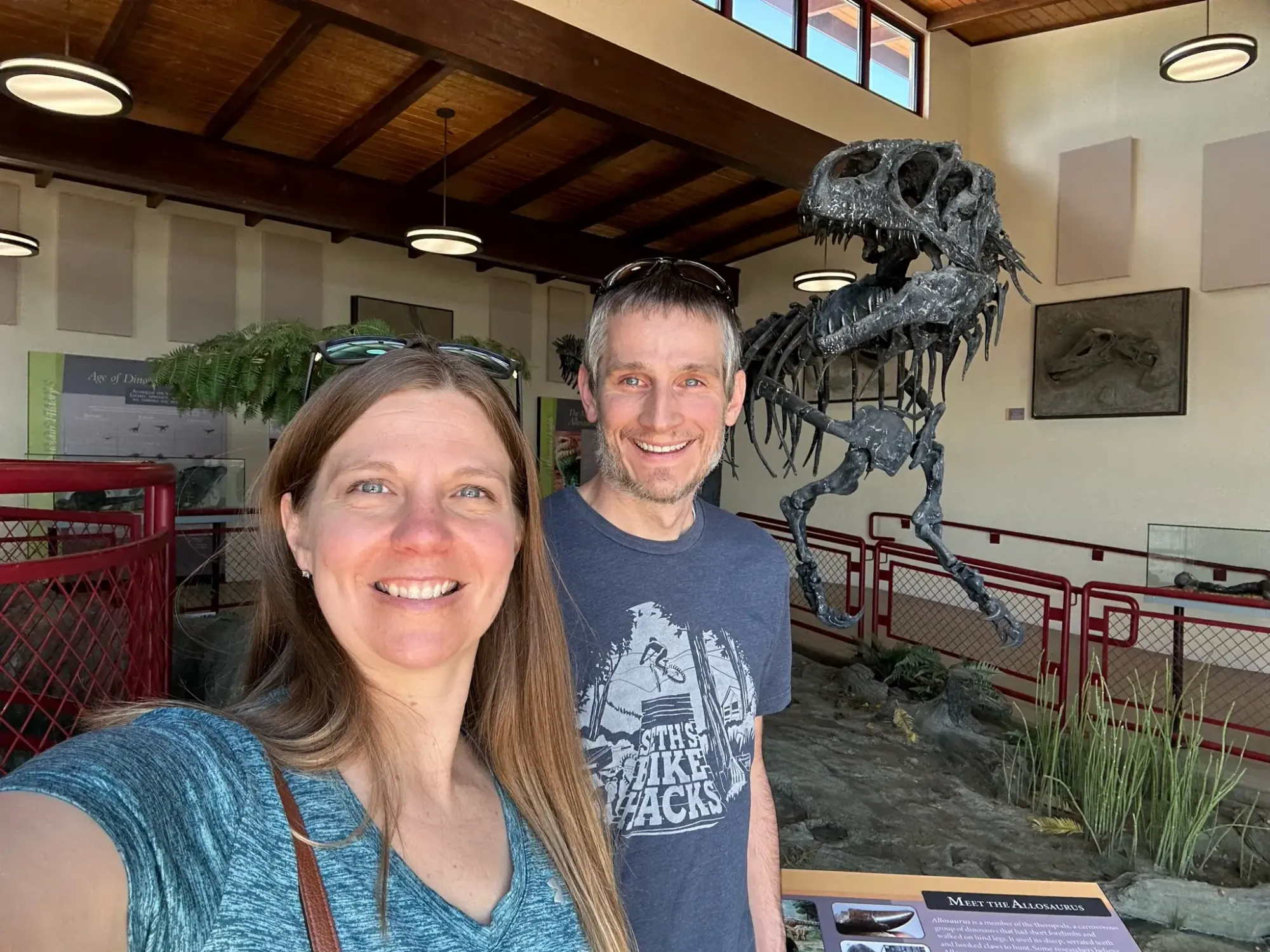 Keith and Lindsey are taking a selfie in front of a large dinosaur replica