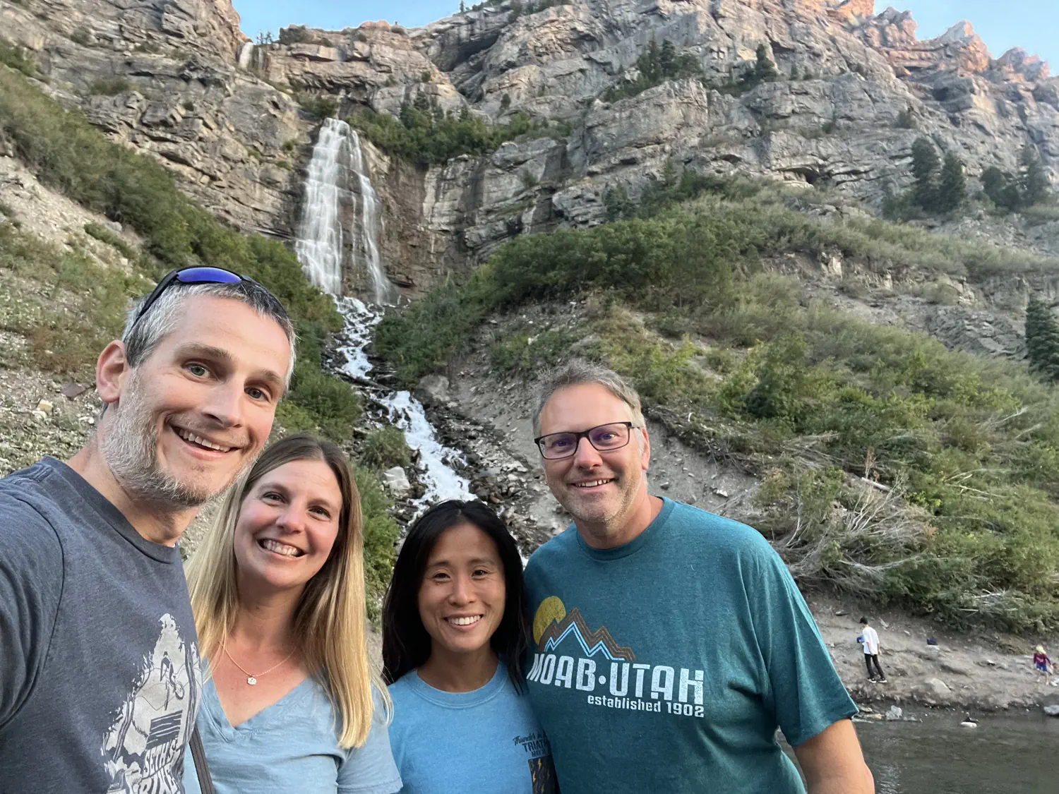 Keith, Lindsey, Priscilla, and John are taking a selfie in front of Bridal Veil Falls in Provo, UT