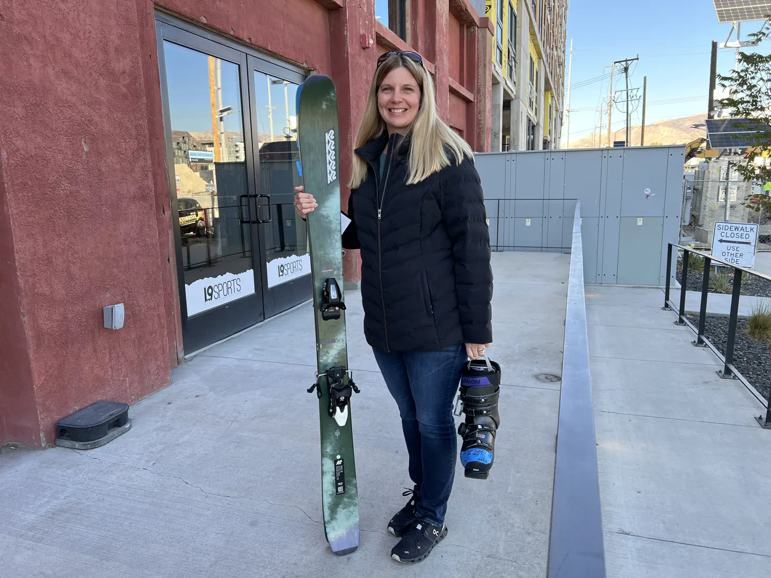 Lindsey is posing with her new skis and ski boots in front of Level Nine Sports in Salt Lake City, UT