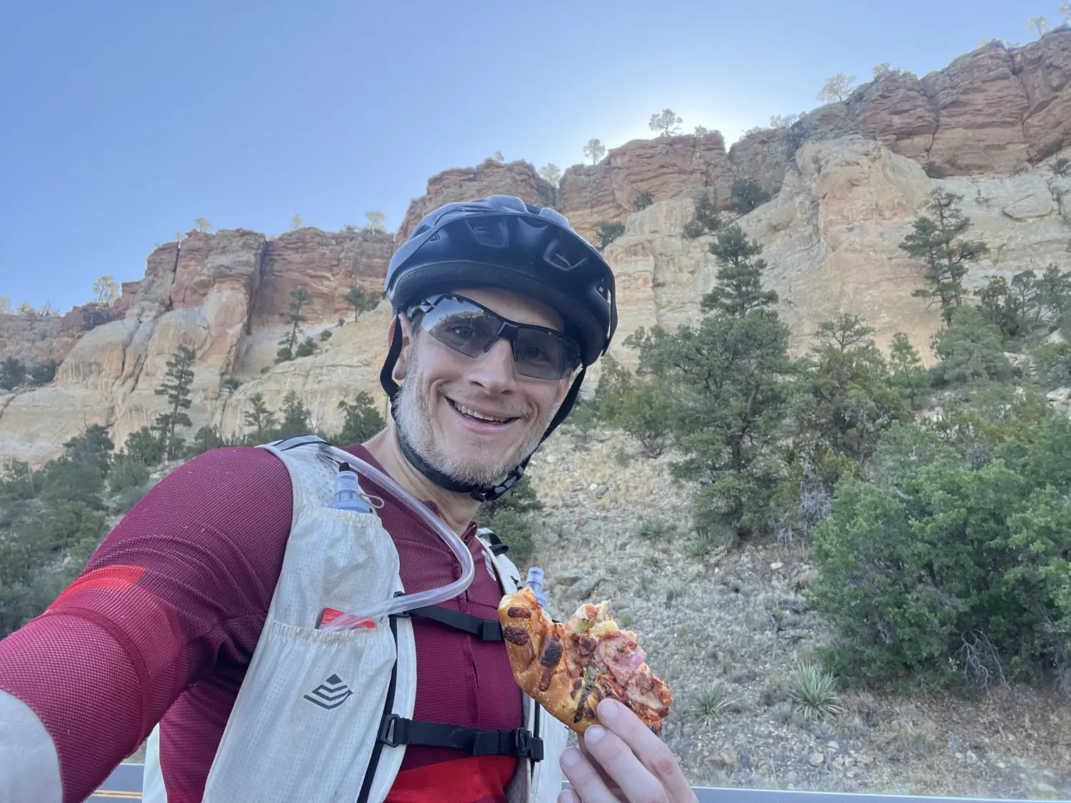 Keith is wearing his Semsty Running Hydration Vest while eating a slice of pizza on the side of the road